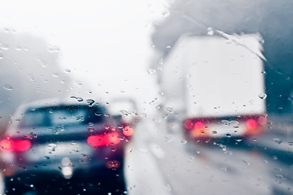 a rain covered windshield with cars driving down the road
