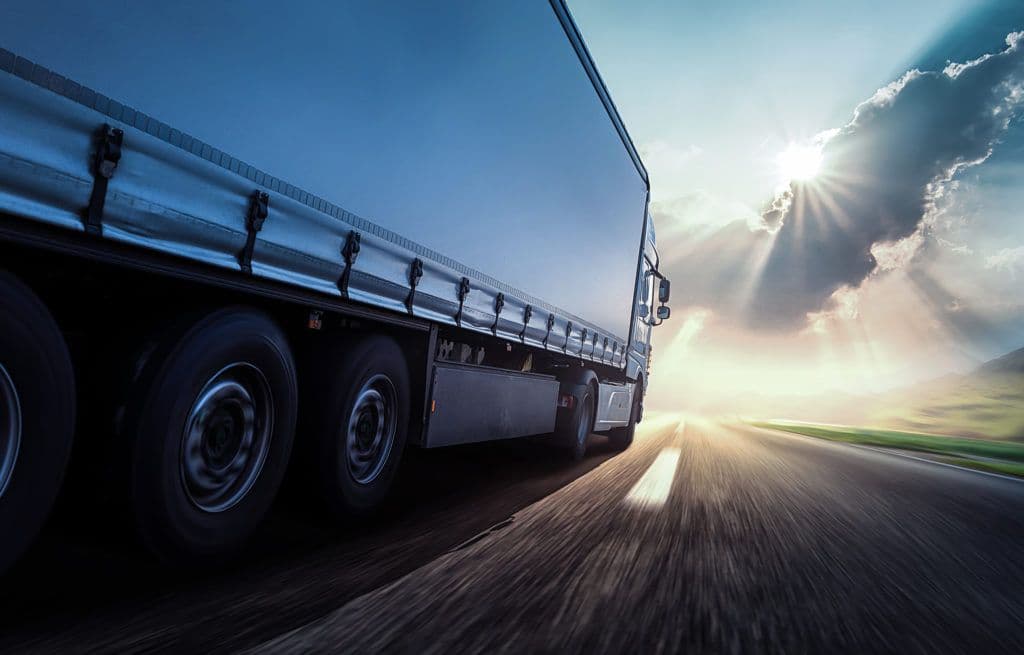 a truck driving down a road with the sun shining down