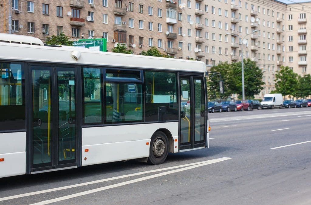 a white bus driving down a street next to tall buildings