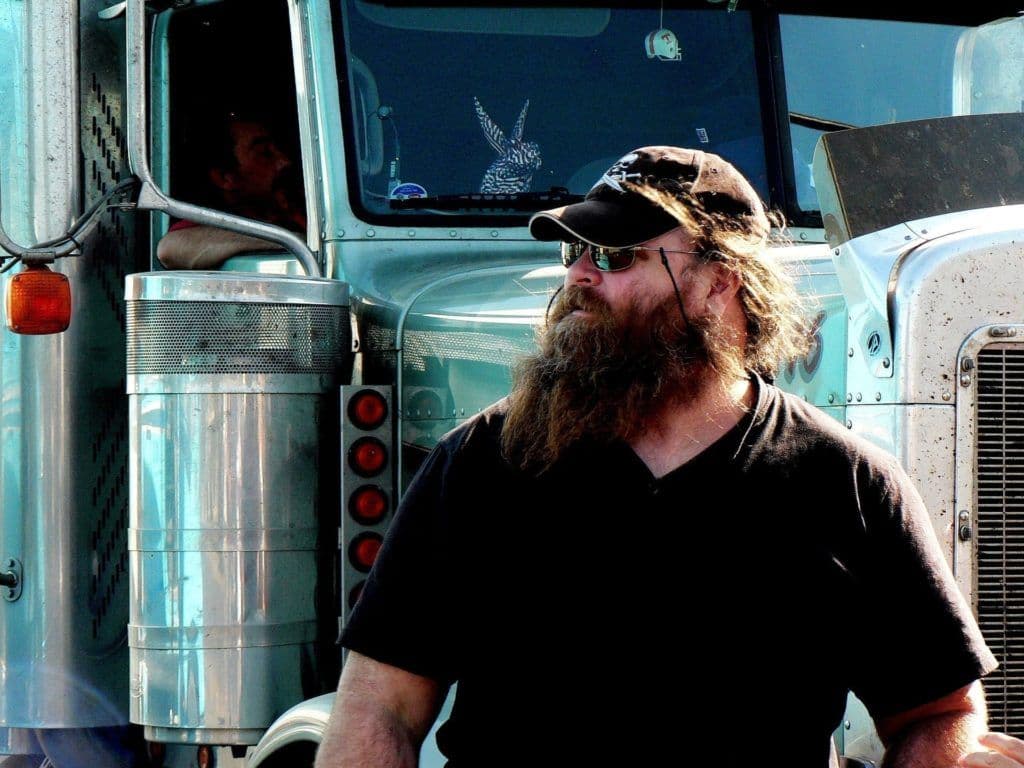 a man with a long beard standing in front of a truck