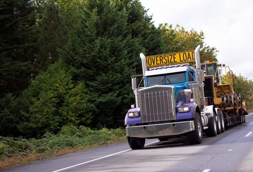 a large truck driving down a road next to a forest