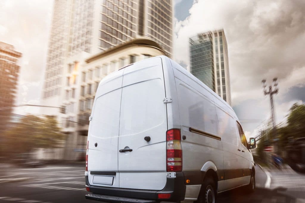 a white van driving down a street next to tall buildings