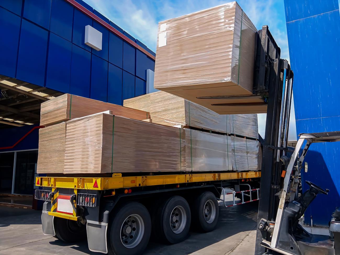 Forklift loading wrapped cargo onto a flatbed truck trailer