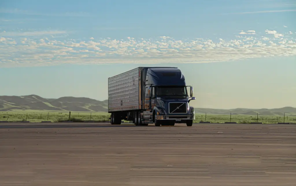 A semi truck on an open road with green hills under a blue sky