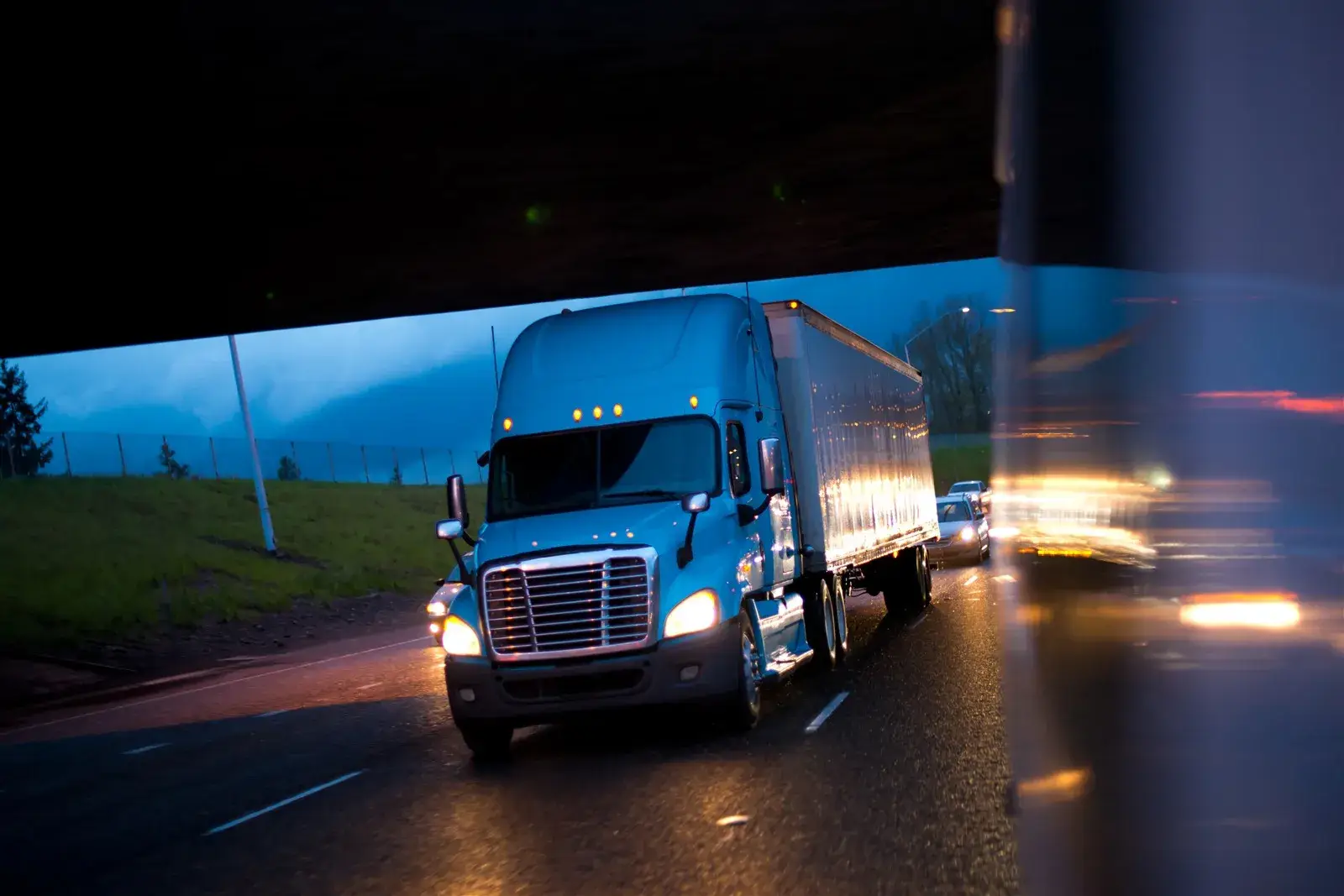 Semi-truck with headlights on driving on a wet highway at night