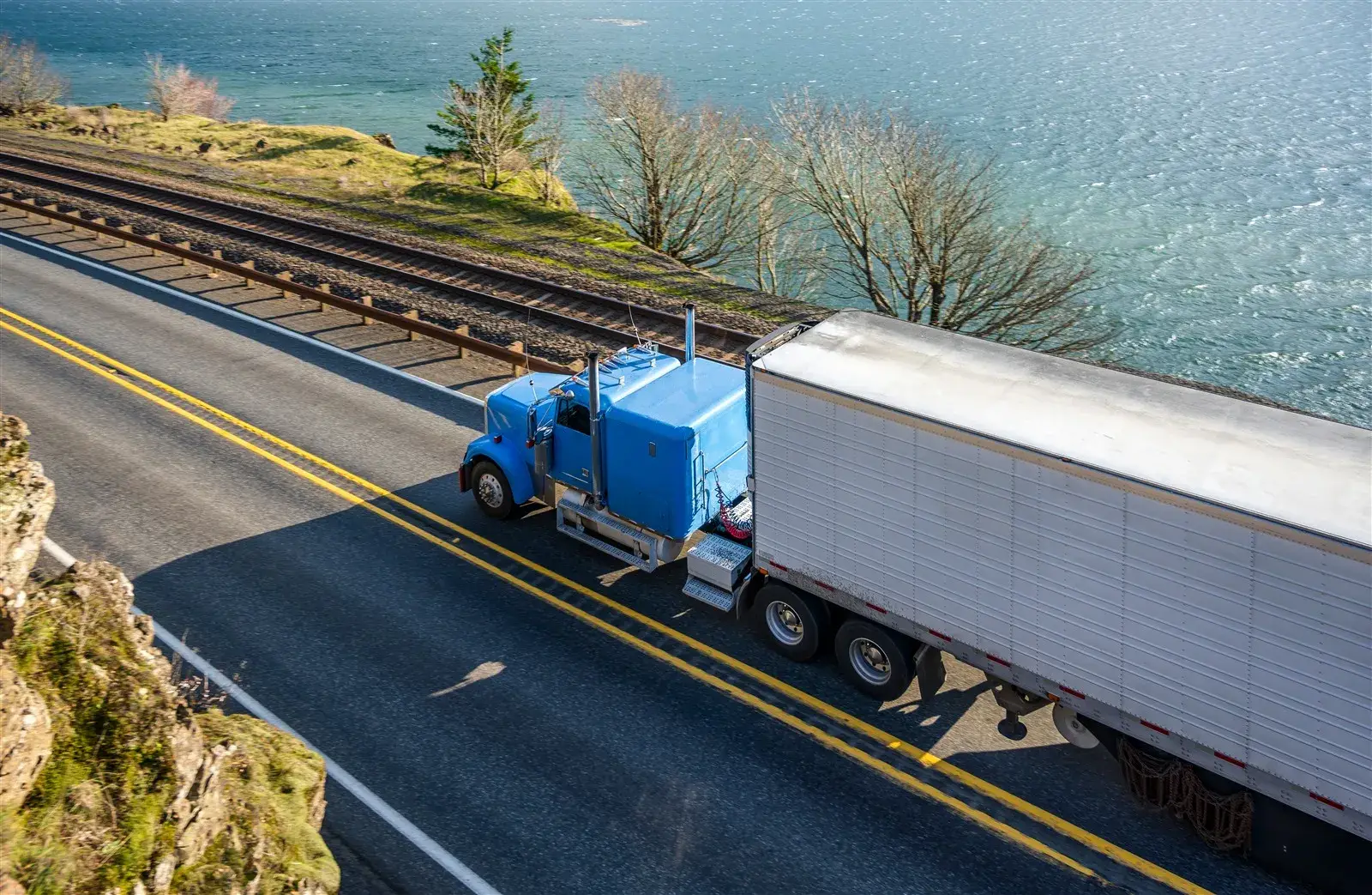Blue semi-truck with a refrigerated trailer on a highway along the Columbia River