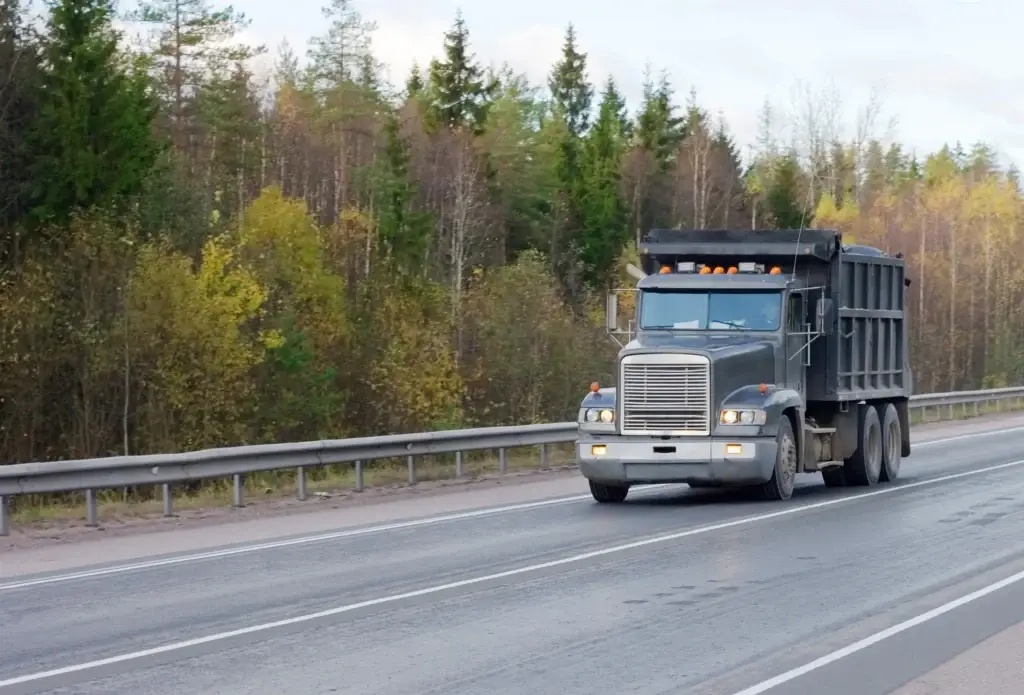 Dump truck driving on a highway lined with evergreen trees