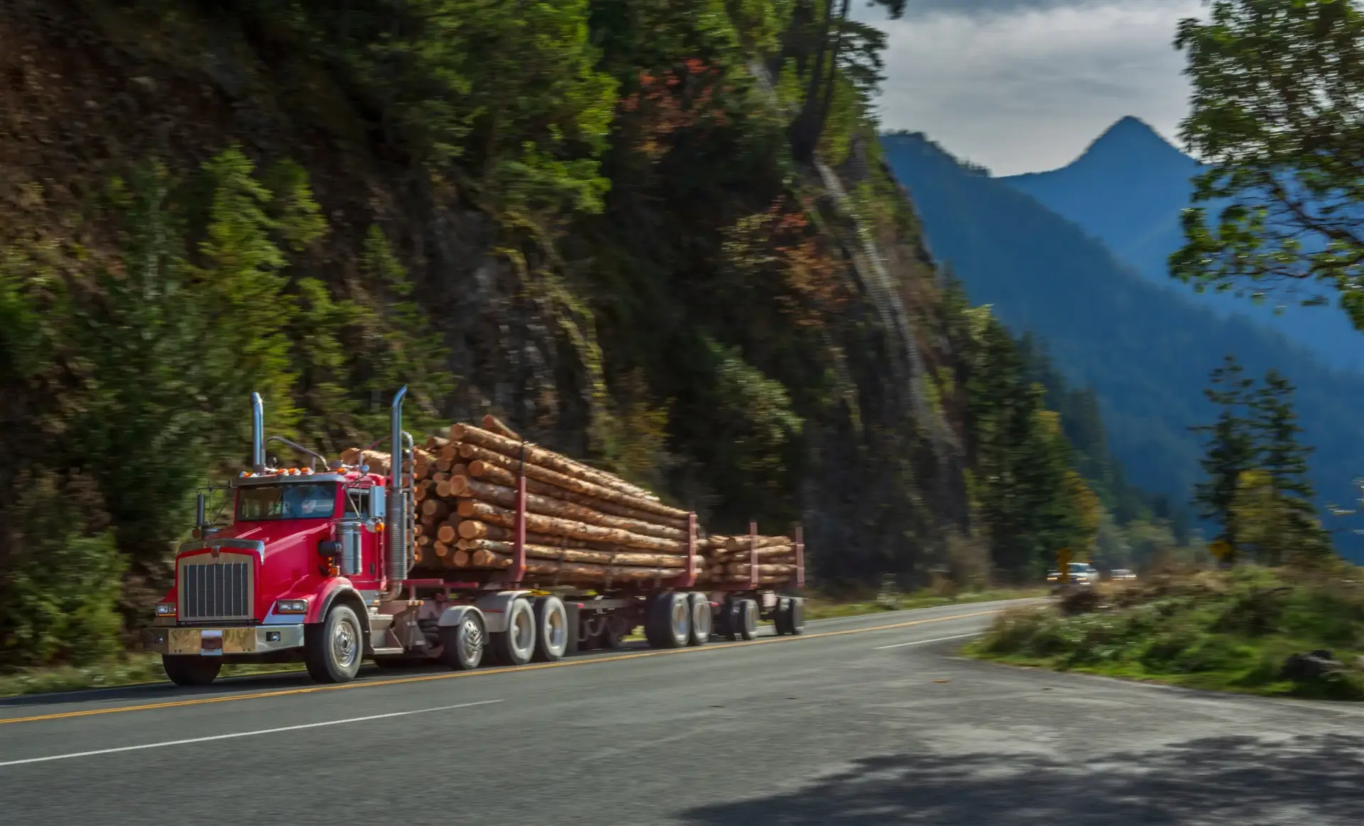 Red logging truck hauling timber on a curving mountain highway