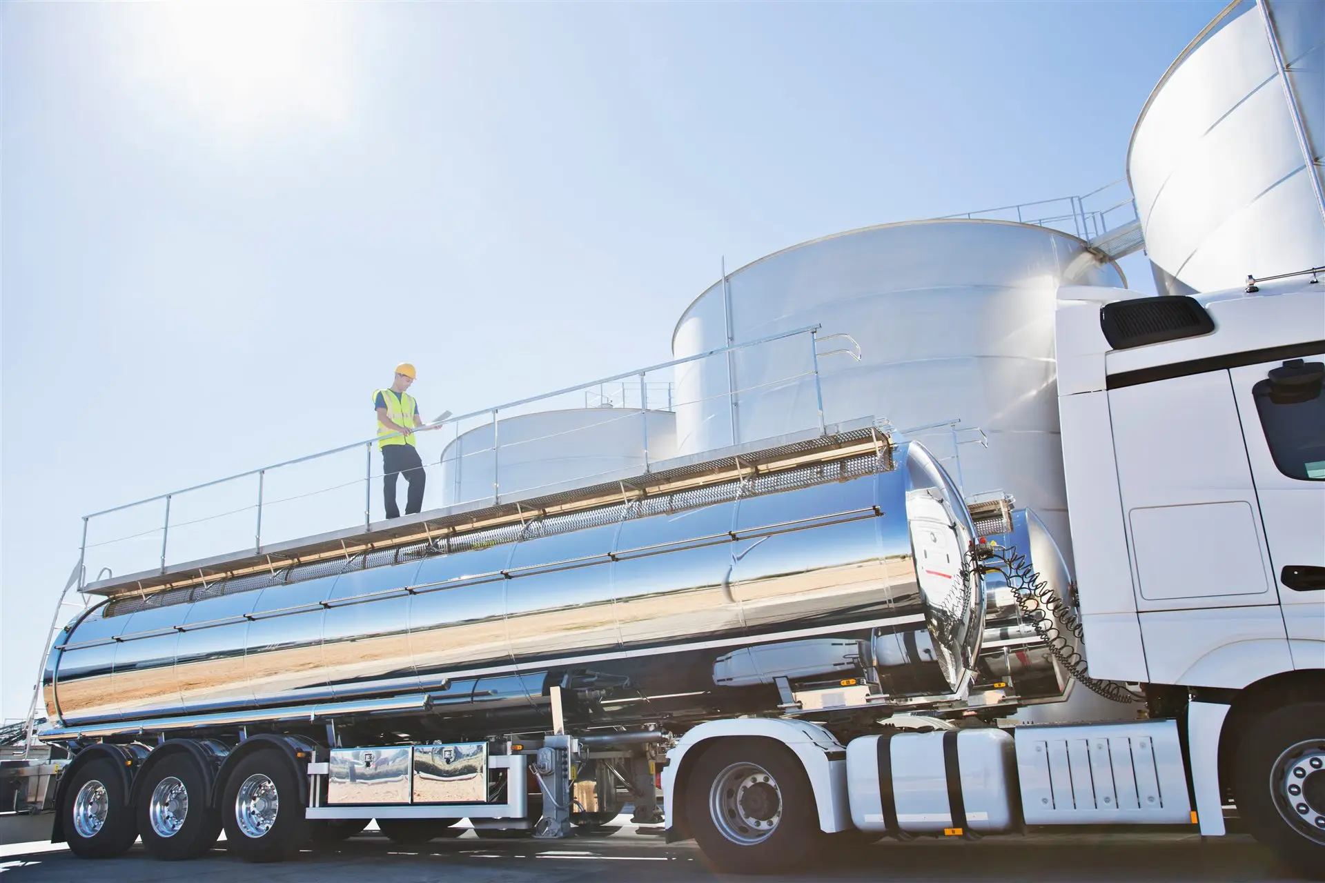 Worker standing on top of a stainless steel tanker trailer at a loading facility